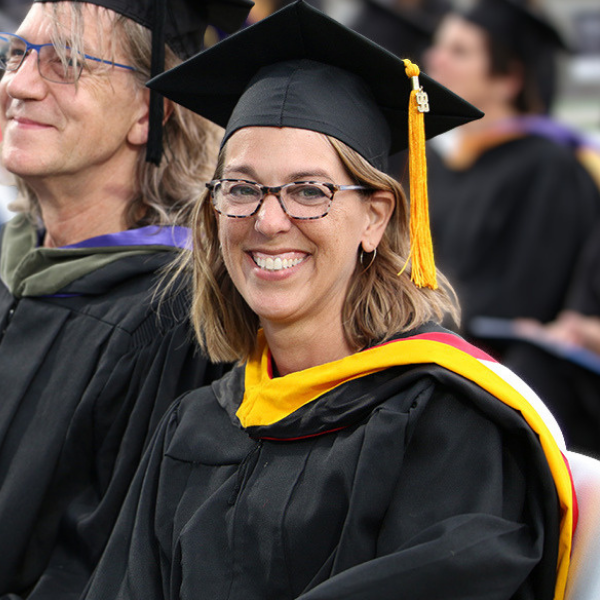 Professor Angela Redmon wears graduation regalia and sits among other faculty members at a graduation ceremony.