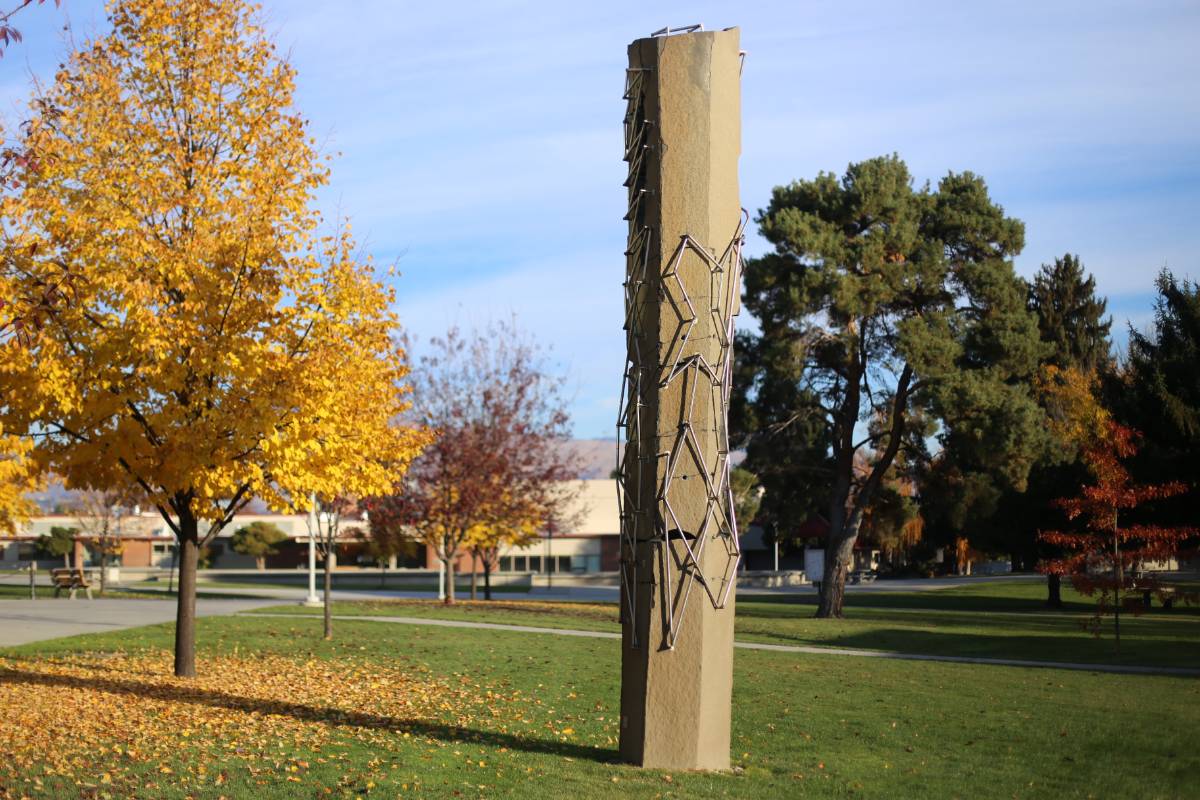 Tall pillar-like sculpture on Wenatchee Campus with fall foliage adjacent