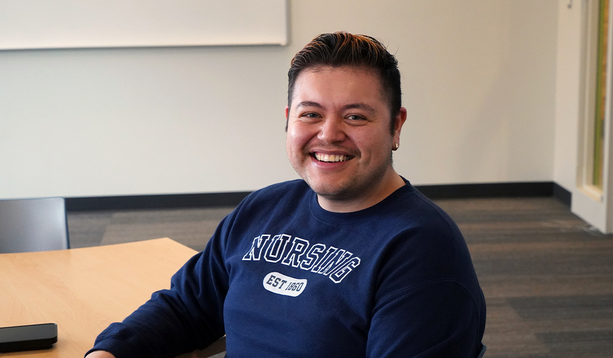 A WVC nursing student sits at a table in a classroom wearing a blue sweatshirt with "nursing" printed across the front.