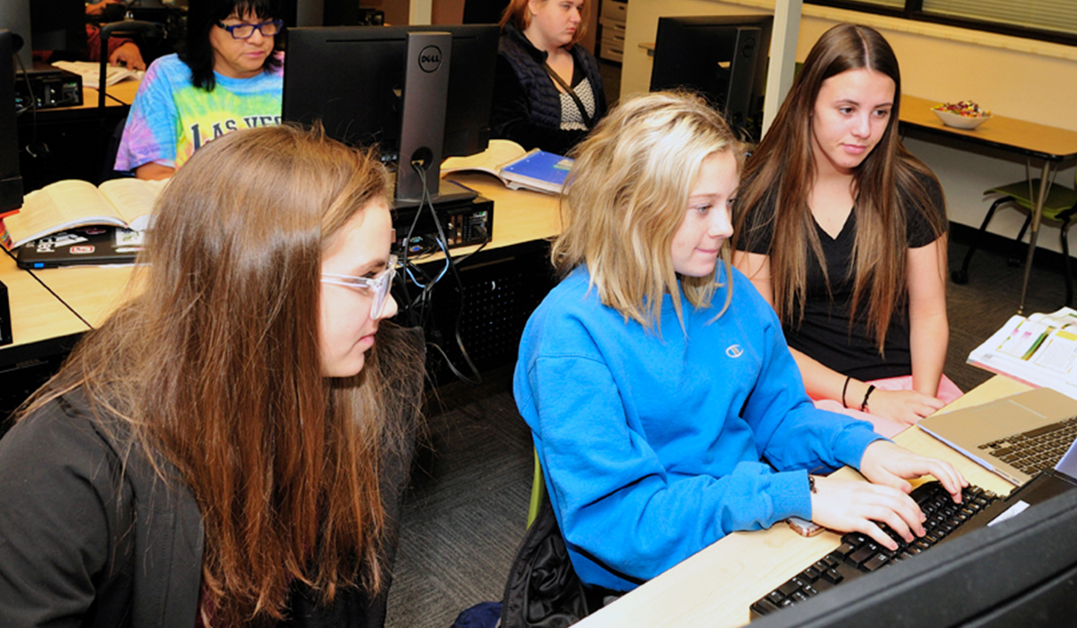 Three Business Computer Technology students work on a computer project together.