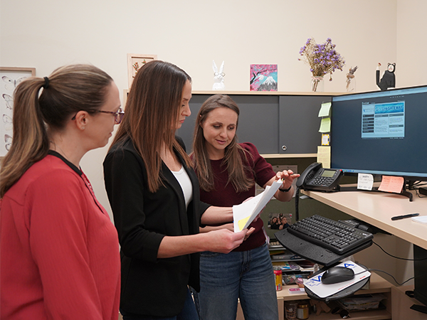 Three office staff members study a document together.