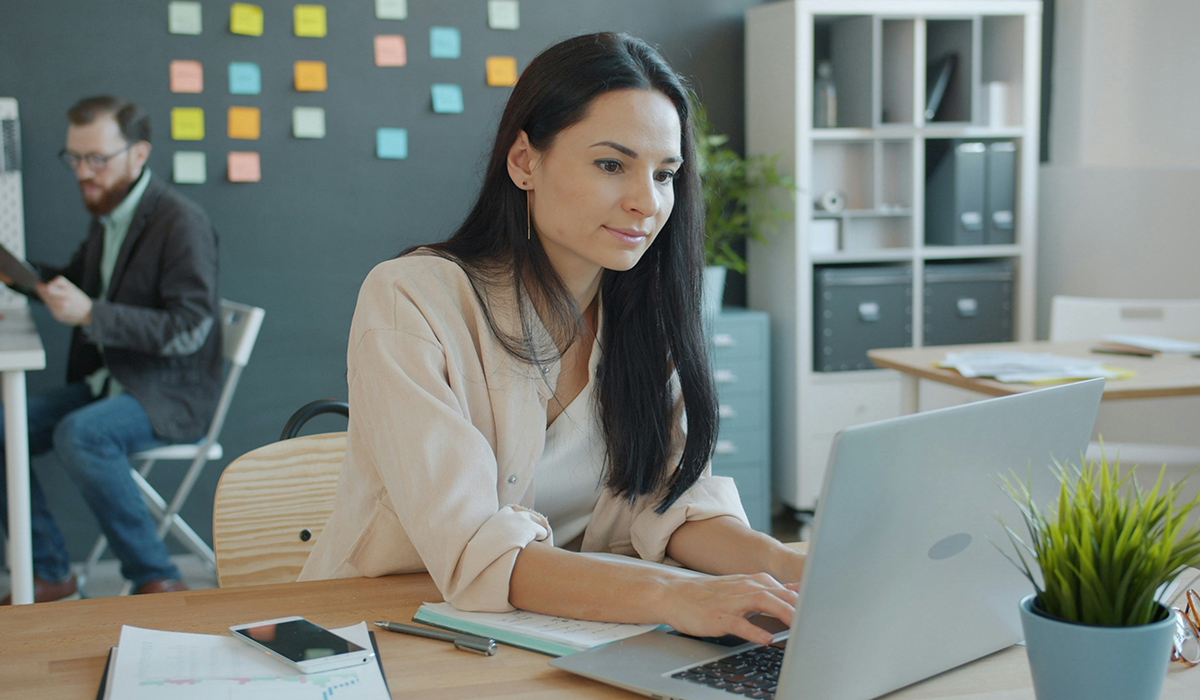 A woman sits at a desk and works on a laptop.
