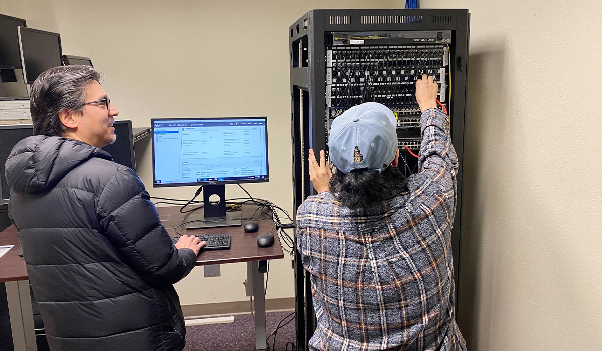 A student works on a computer network while the instructor observes.