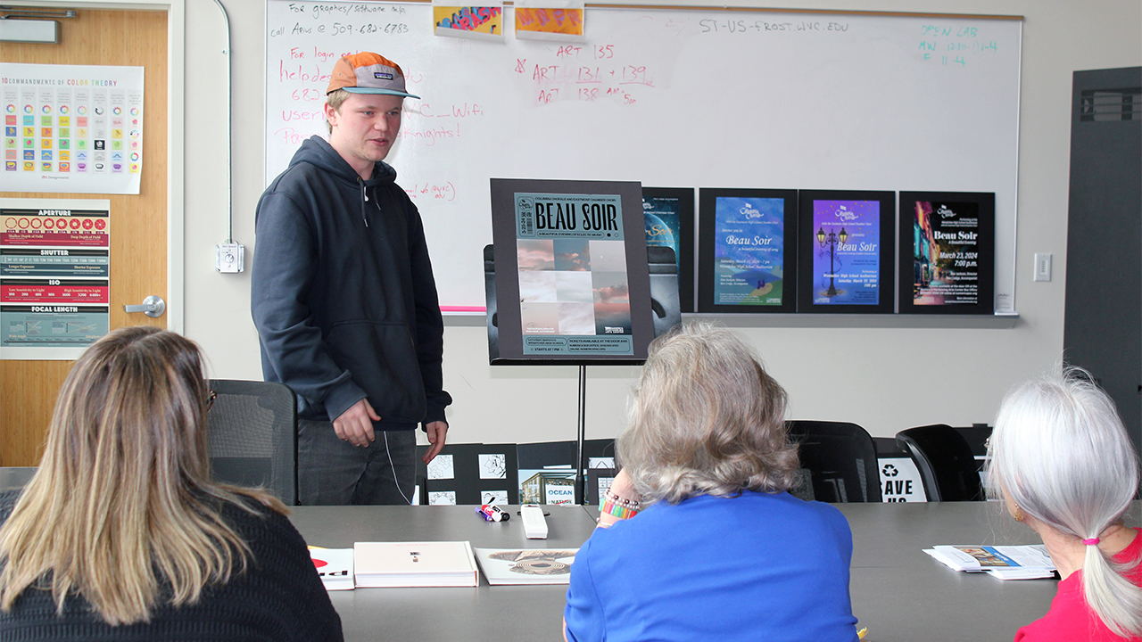 A group of women observe a poster that a graphic design student has created.