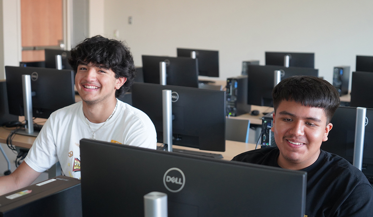 Two students sit at computers in a classroom.