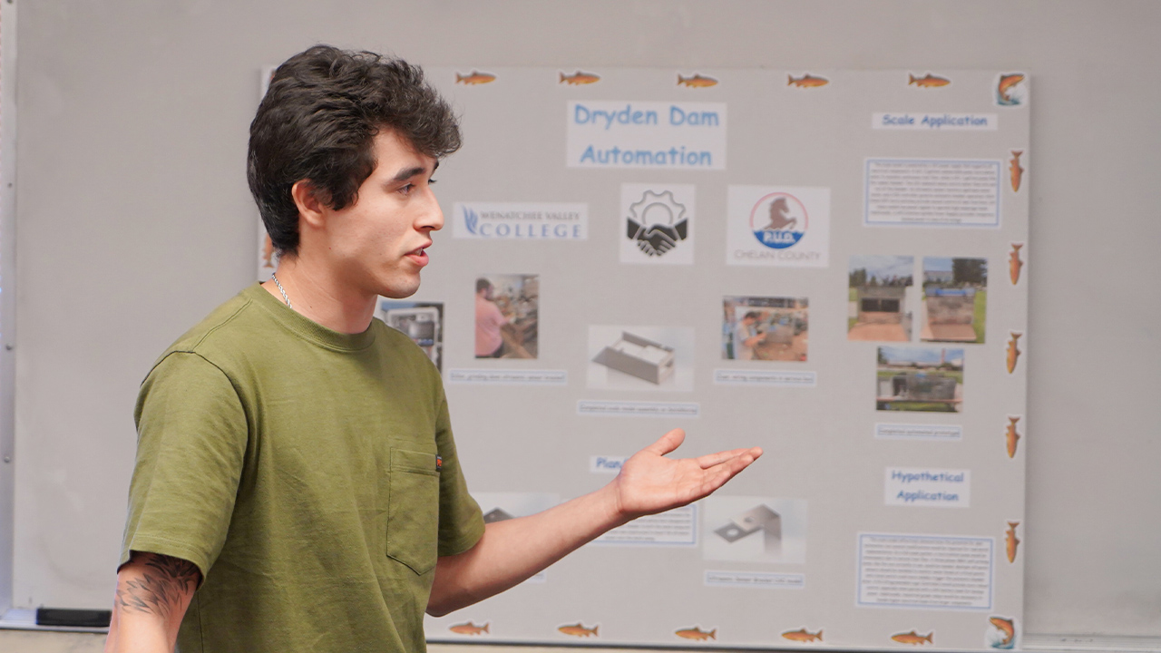 An engineering student stands in front of a poster that describes a dam automation project.