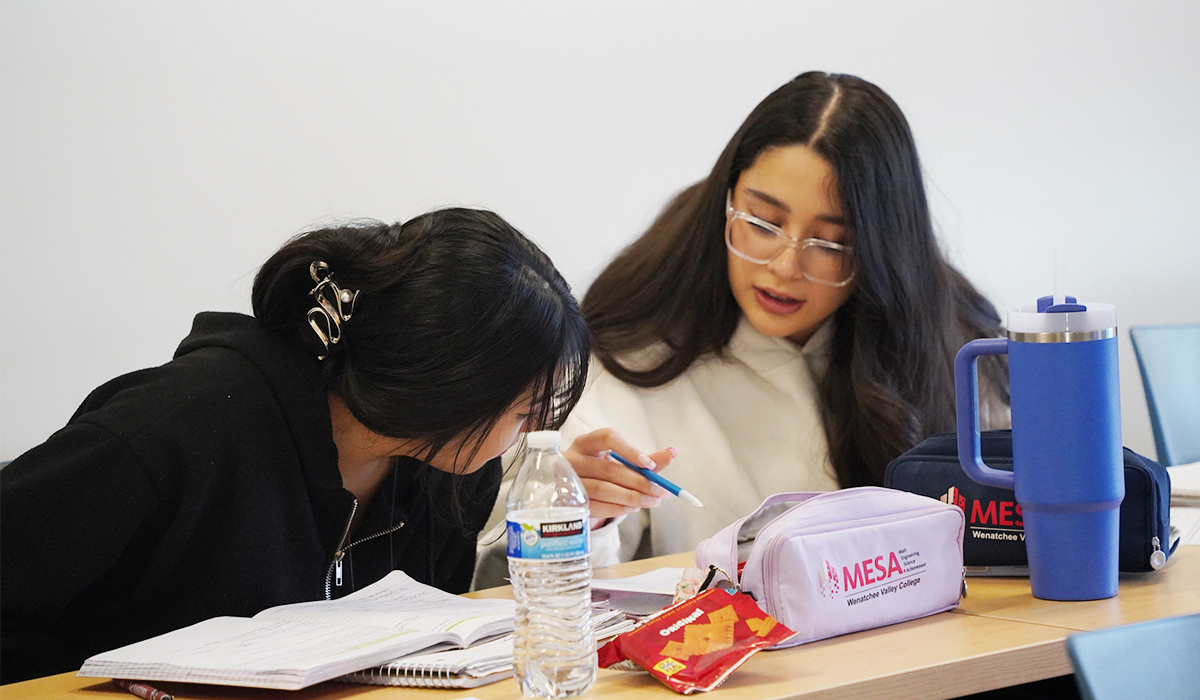 Two students sit at a table with a MESA program pencil pouch in front of them.