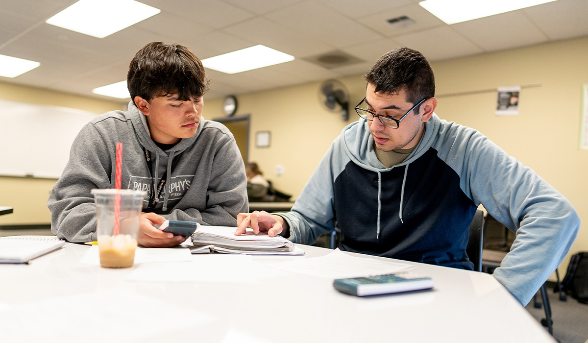 Two math students sit at a table and work on a problem together.