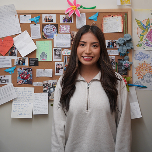 Magali Olguin-Ramos stands in front of a corkboard covered in thank-you notes.