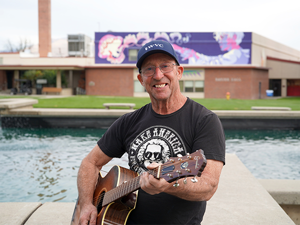 Tom Martin stands near the Wenatchee campus fountain while holding his guitar.