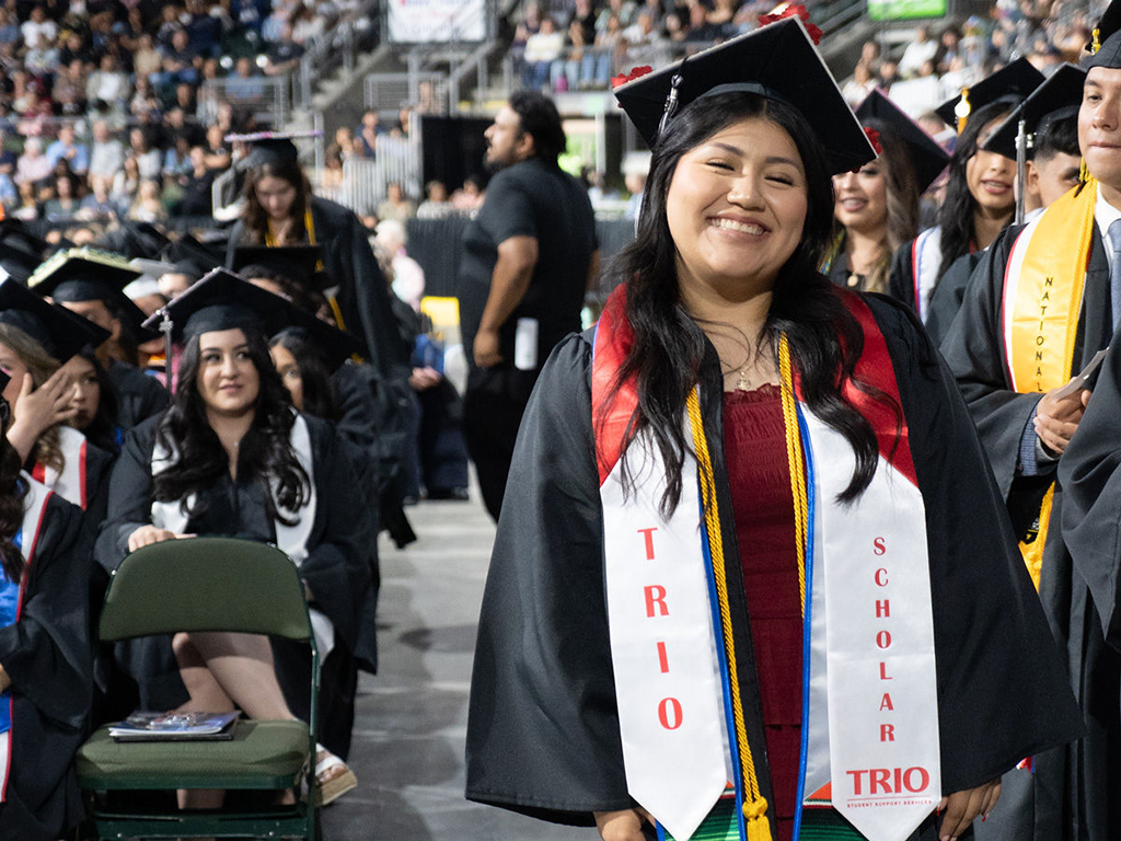 A TRIO student wearing a graduation cap and gown and a TRIO stole.